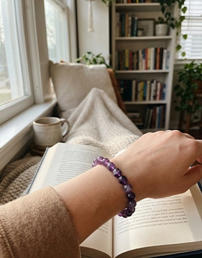 Woman wearing an Amethyst bracelet while reading indoors in a cozy setting