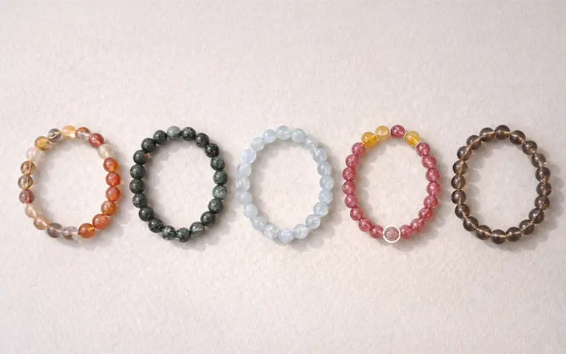 Minimal product-style image of crystal bracelets laid flat, neutral tones, clean background, soft lighting, premium feel