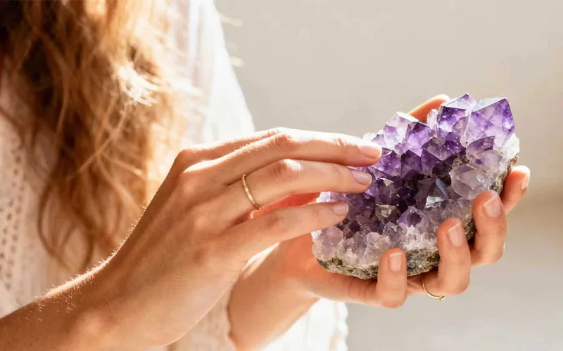 Woman holding a raw amethyst crystal cluster in soft warm lighting